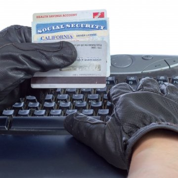 identity theft protection services hands with black gloves on computer typing social security number hands hold social security card